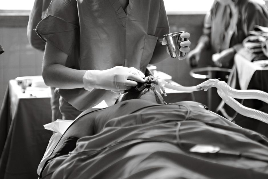 Black and white image of a medical professional performing a procedure in an operating room.