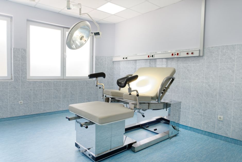 Bright gynecological examination room with adjustable chair and overhead light in a medical facility.