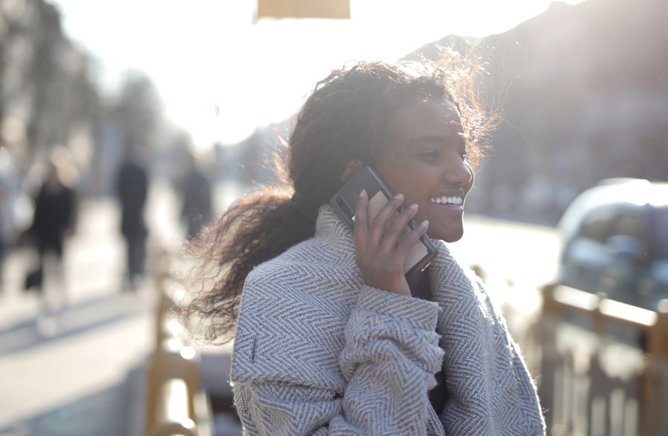 Young woman enjoying a phone call while walking outside on a sunny day.