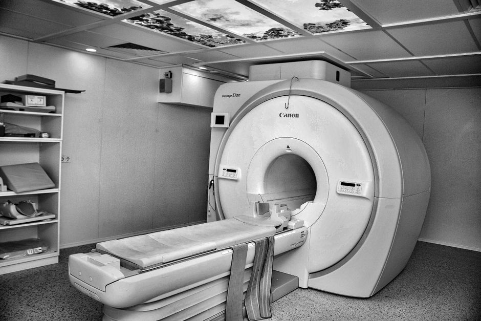 Black and white image of a modern MRI machine in a hospital room with overhead ceiling art.